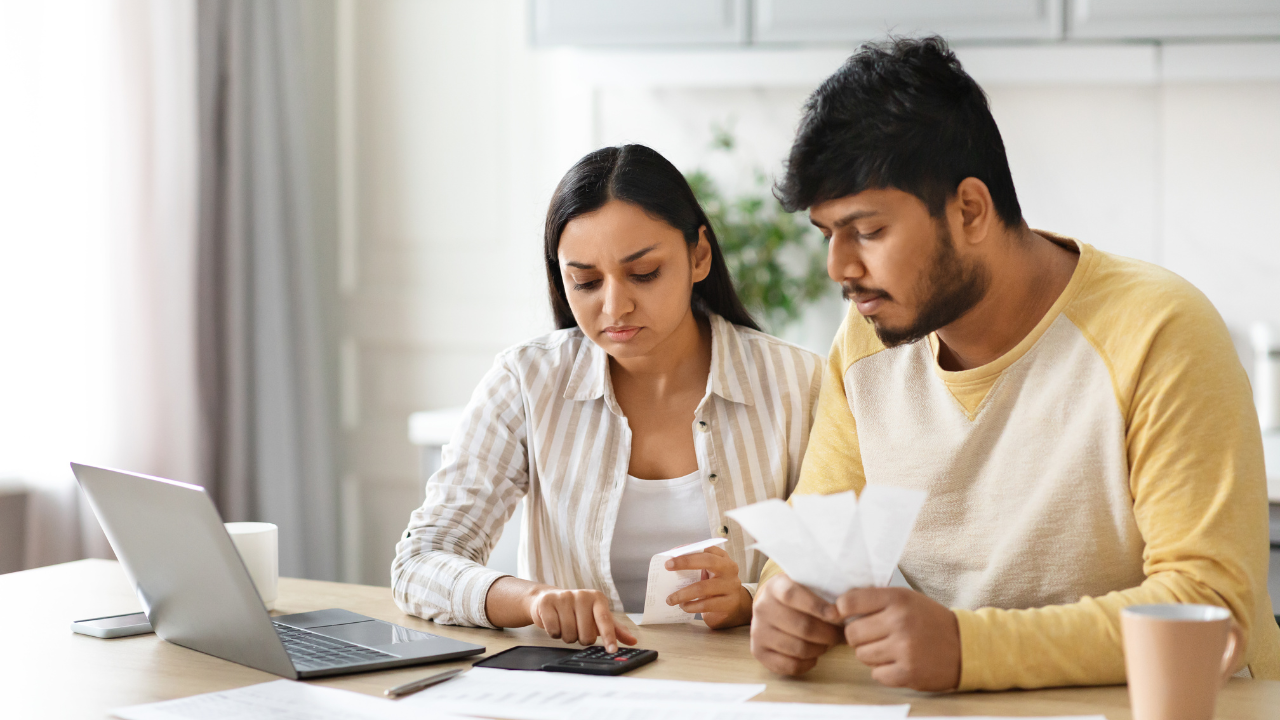 A couple sits at a table with a laptop, calculator, and documents, focusing intently on managing household finances.
