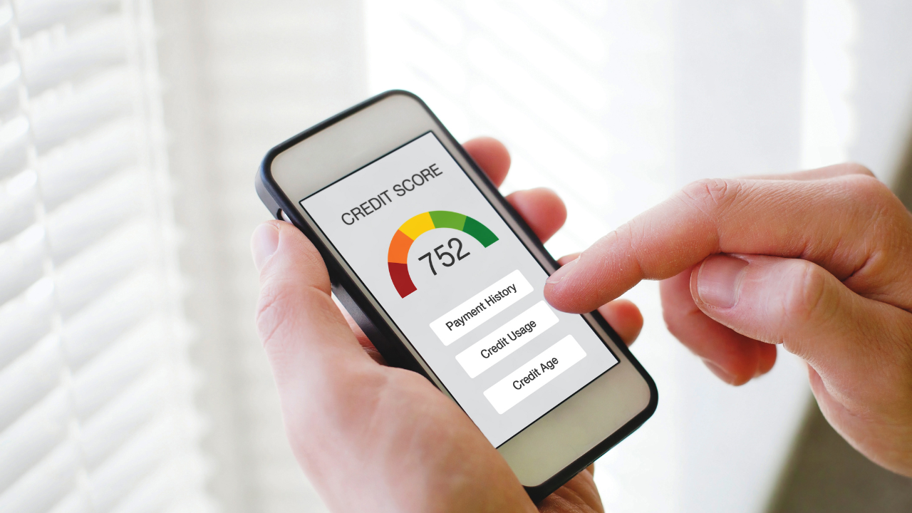 Close-up of hands holding a smartphone displaying a credit score of 752 on a gauge, with a finger touching the screen.