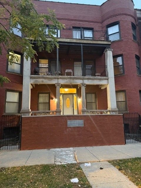 A red brick apartment building with a central entrance, a front porch, and a second-story balcony.