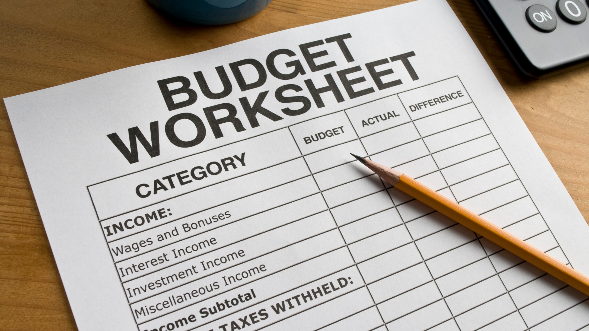 A blank budget worksheet form with columns for budget, actual, and difference, resting on a desk with a pencil and calculator.