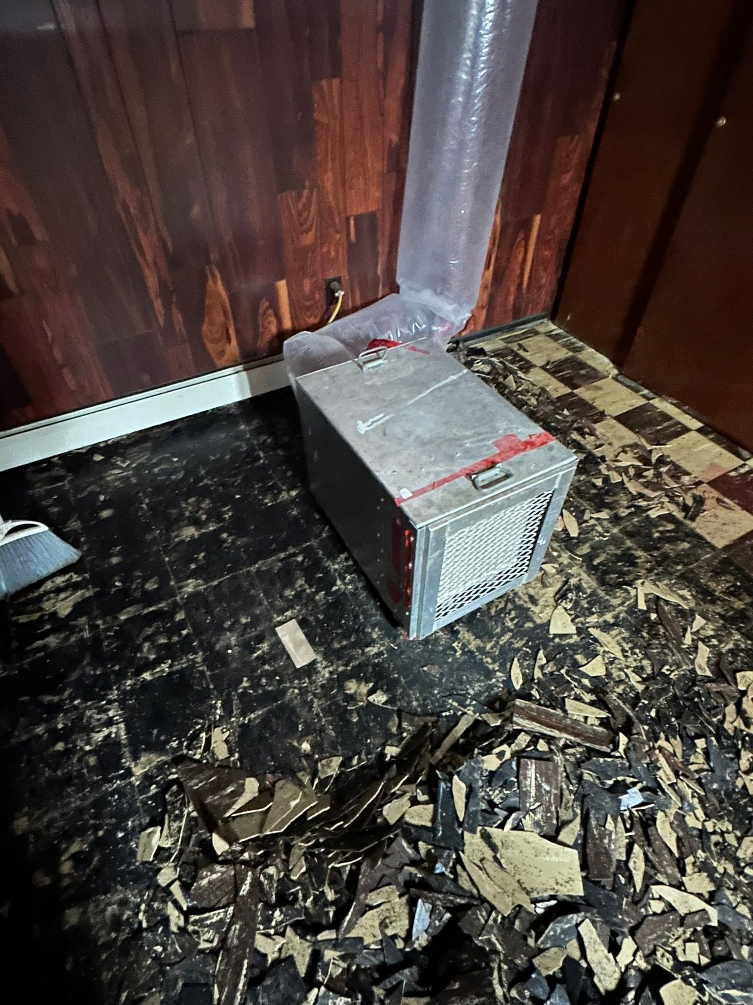 Small damaged metal appliance on a burnt floor beside charred wooden walls.