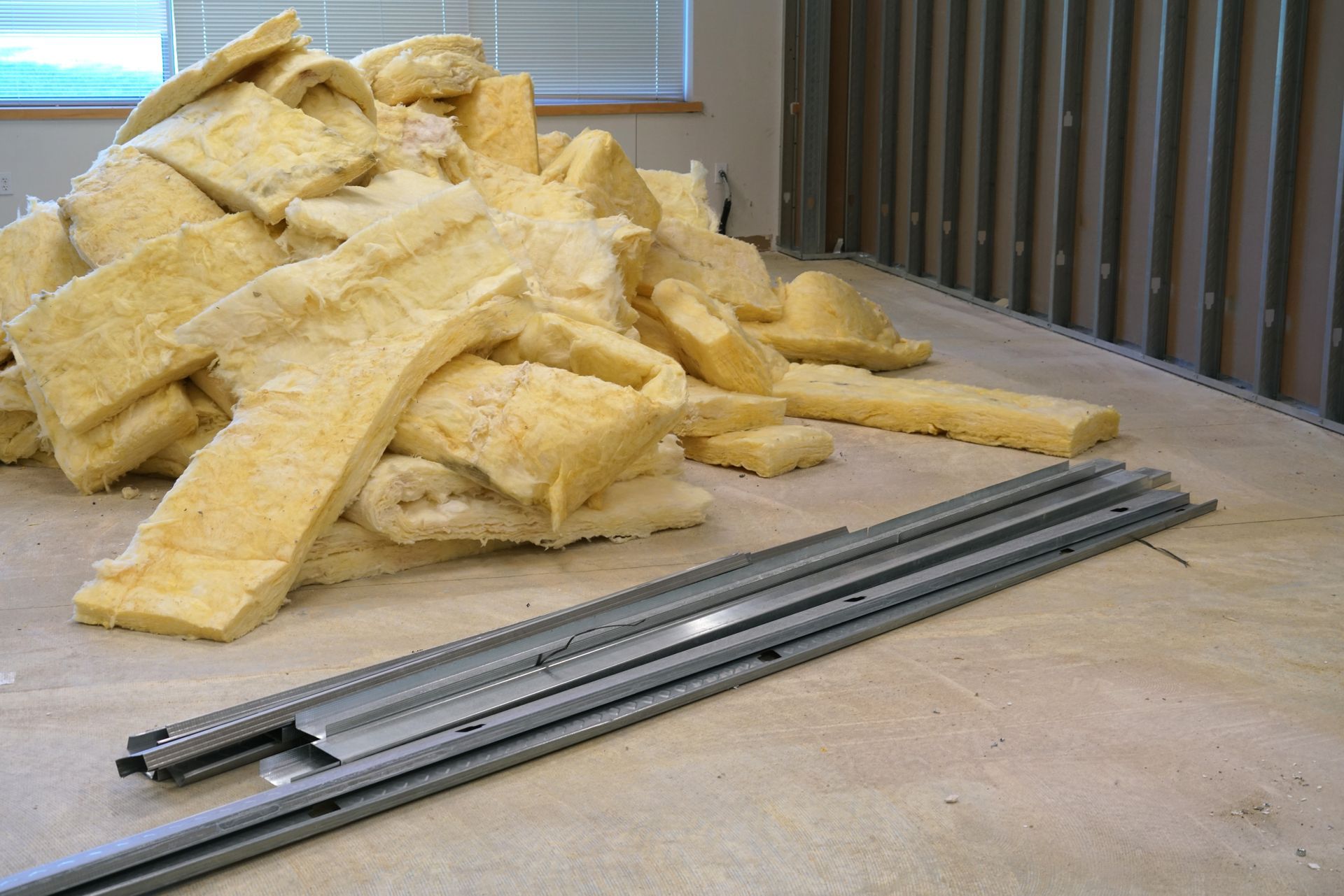 Pile of yellow insulation batts beside metal framing tracks on a concrete floor in a work area