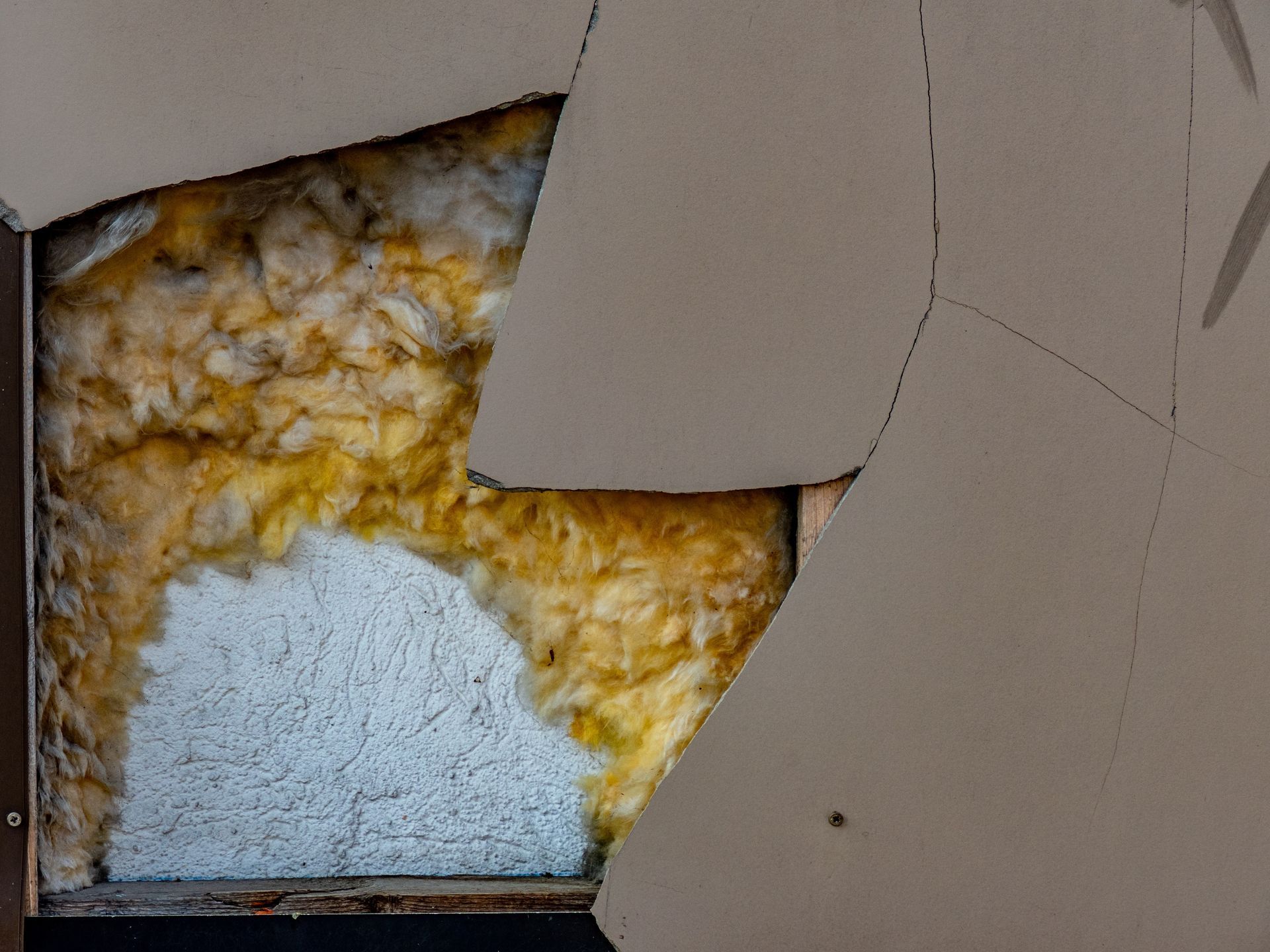 Damaged wall with peeled beige paint revealing yellow insulation and white backing