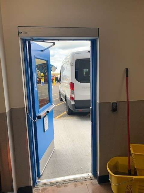 A blue door is open to a parking lot with a white van parked behind it.