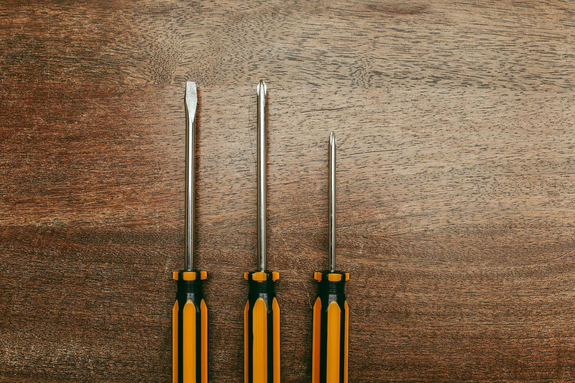 Tres destornilladores con mangos amarillos y negros sobre una superficie de madera marrón.