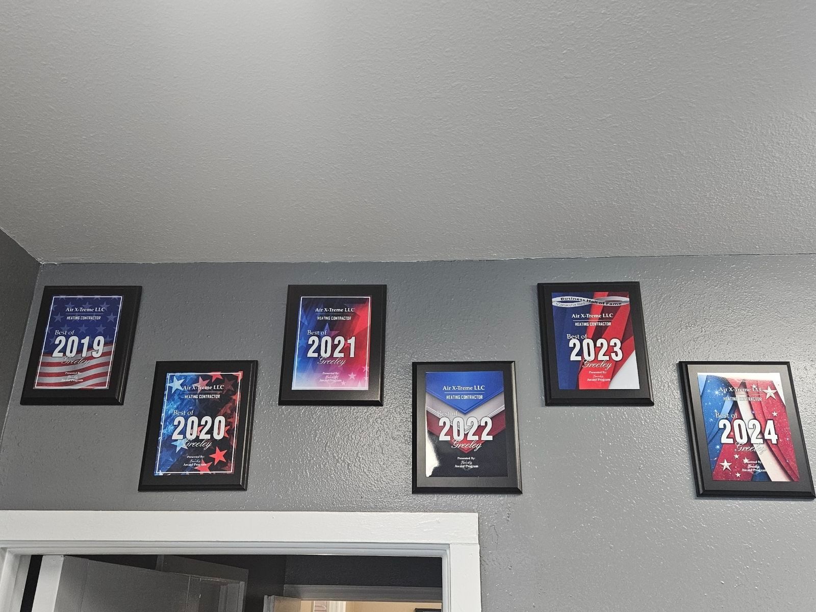 Framed awards with the years 2019-2024 hang on a gray wall above a white doorway.