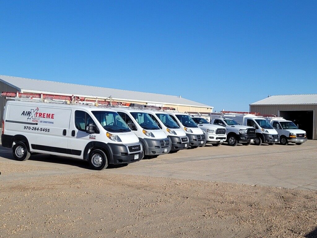 A fleet of white work vans parked in a gravel lot, under a clear blue sky.