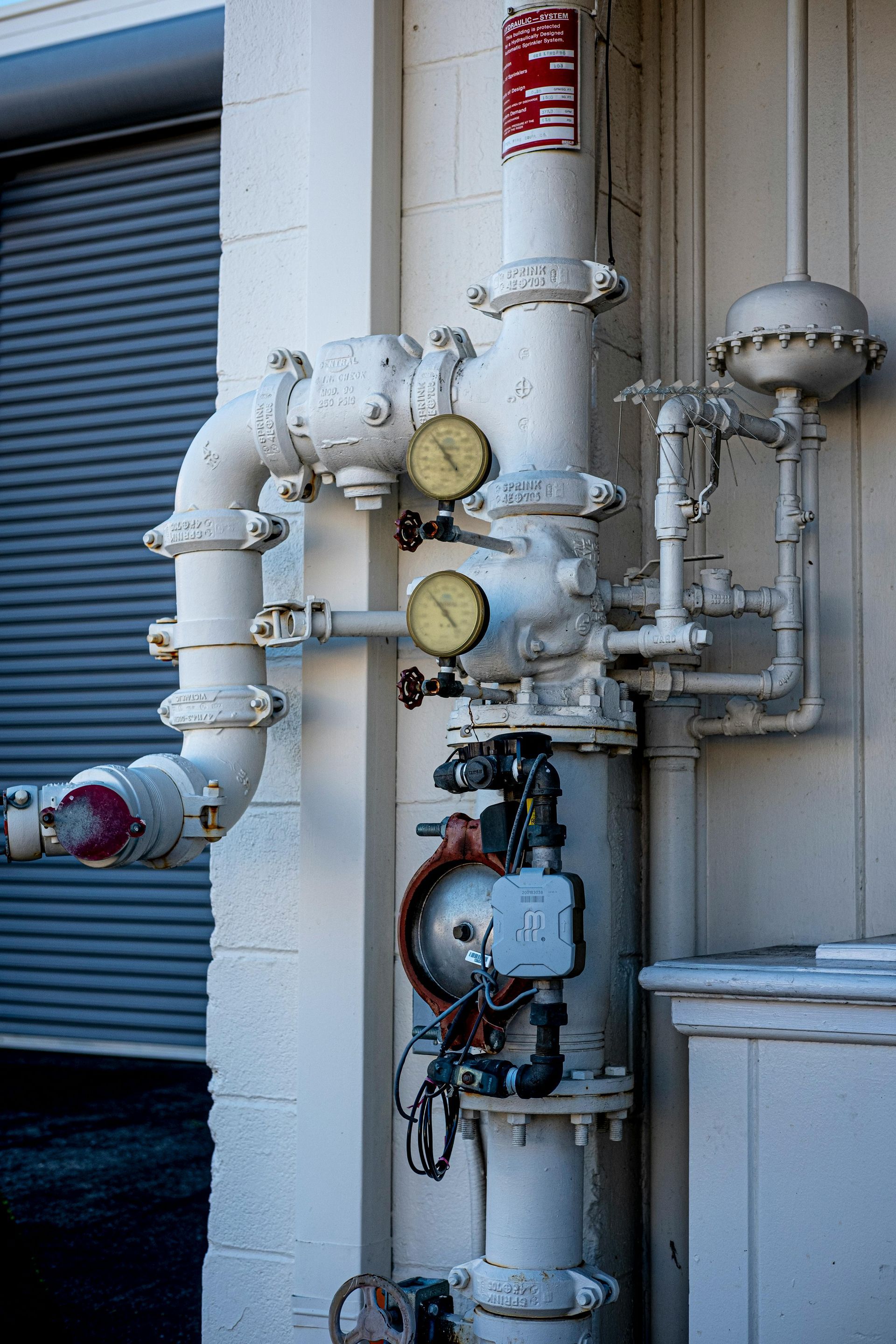 White industrial pipes and gauges attached to building exterior.