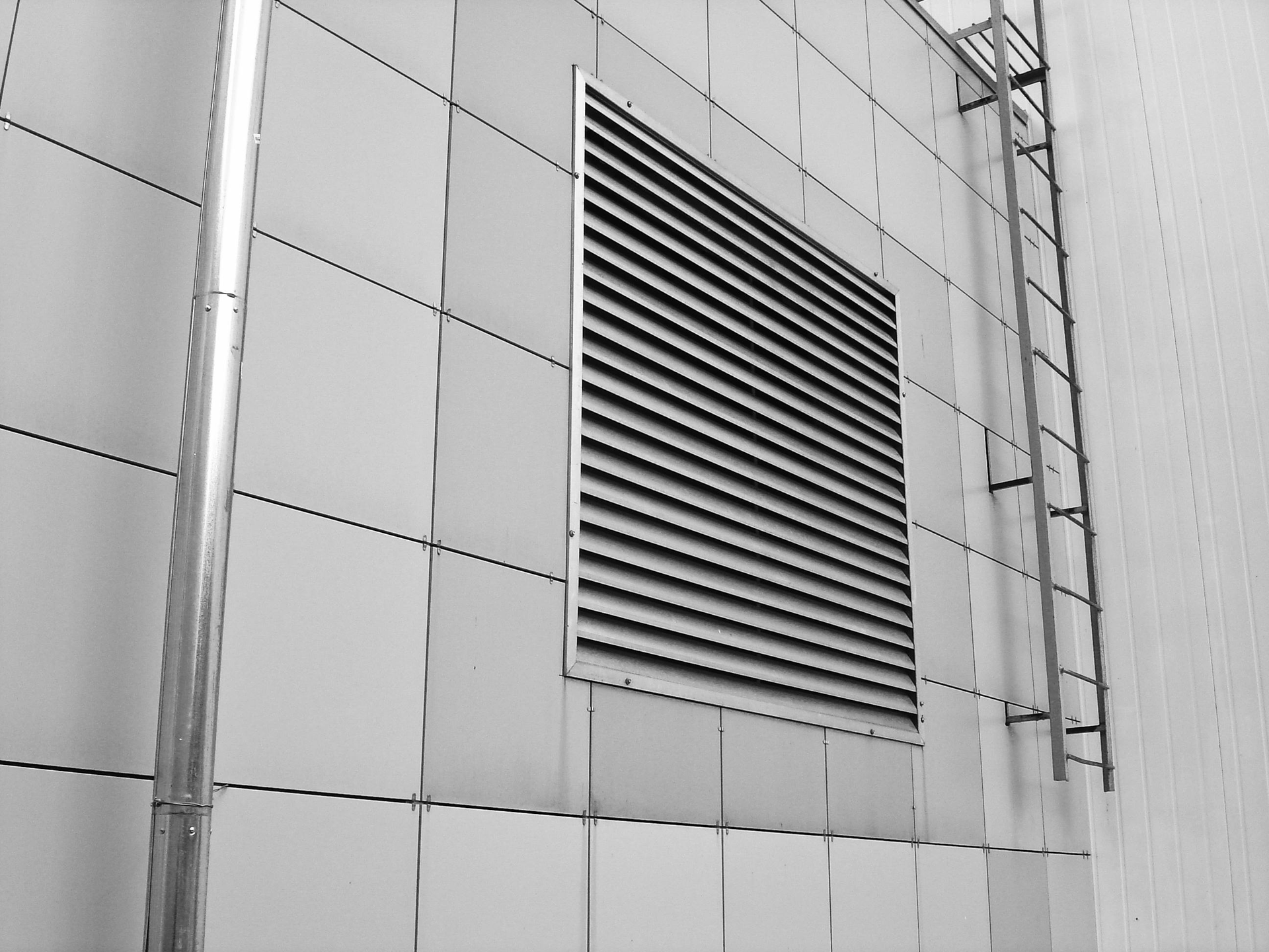 Metal wall with a square vent and a ladder attached.