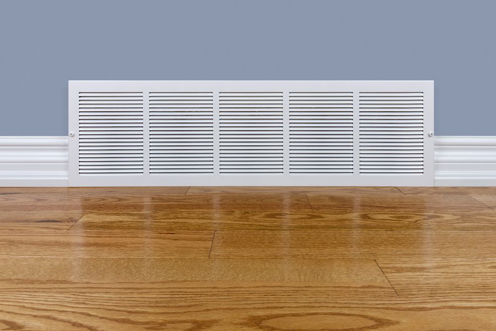 White air vent on wood floor against a blue wall and white baseboard.
