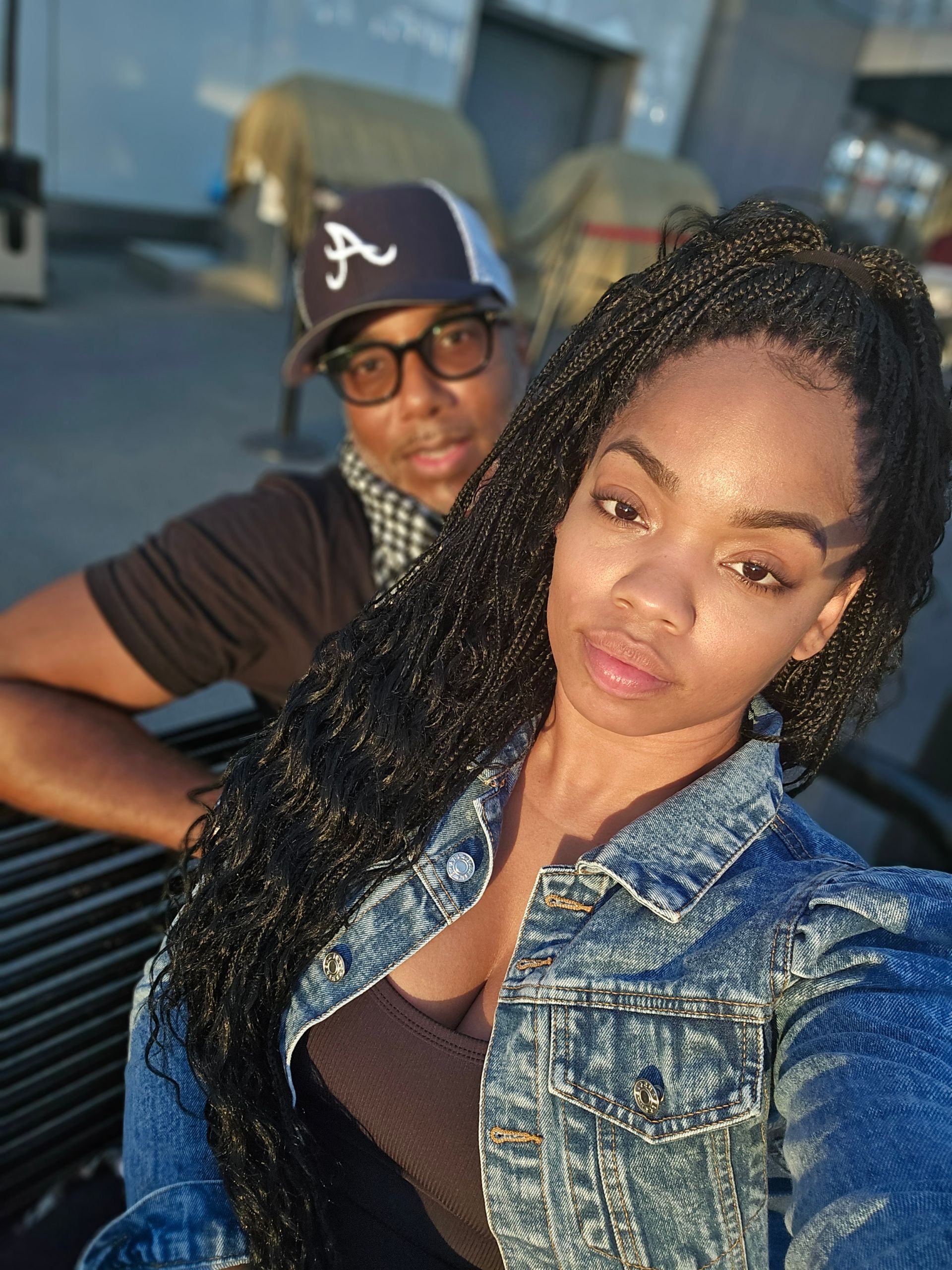 A man wearing a hat with the letter a on it is standing next to a woman wearing a denim jacket