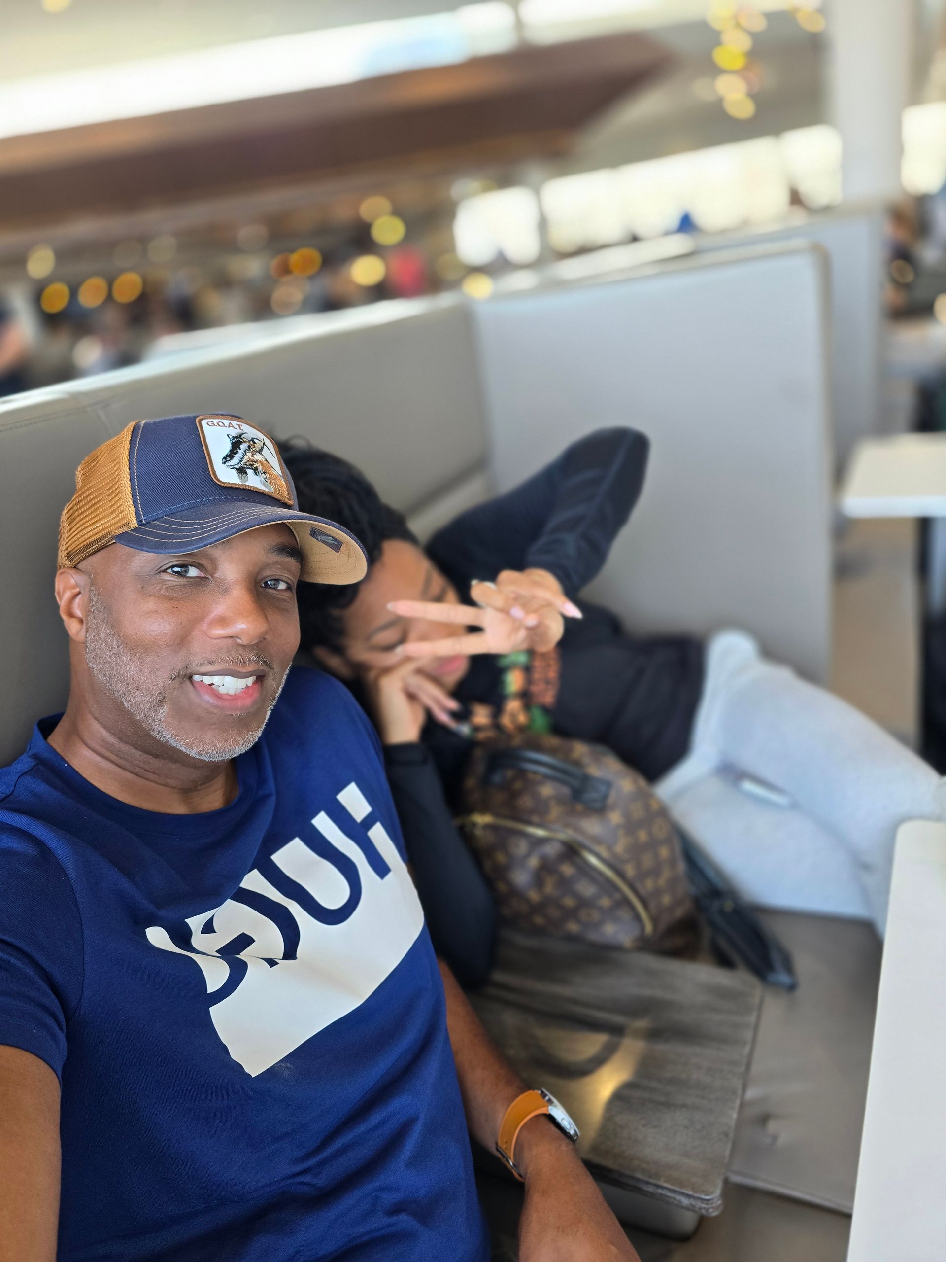 A man and a woman are sitting on a couch at an airport.