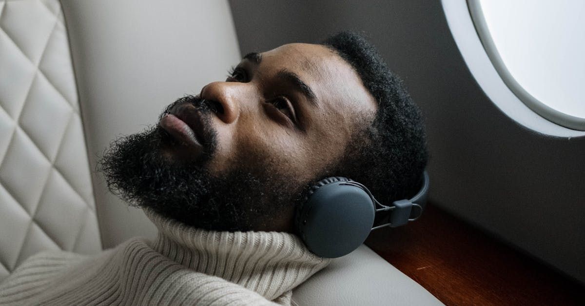 A man with a beard is wearing headphones on an airplane.
