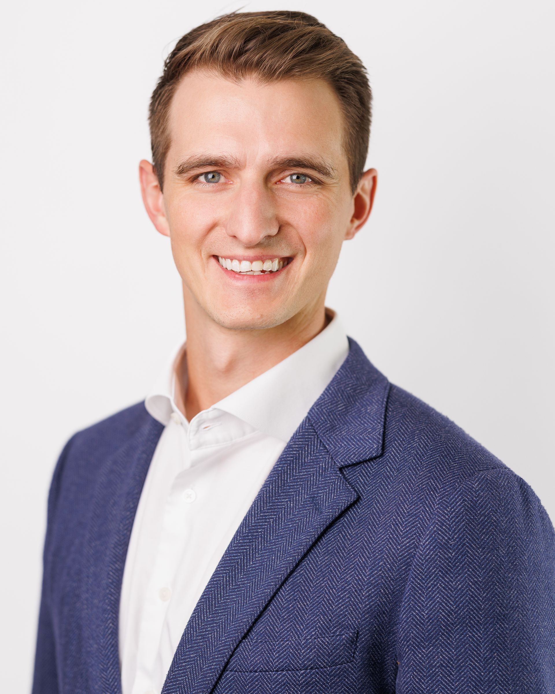 Man in blue blazer and white shirt smiling at the camera.