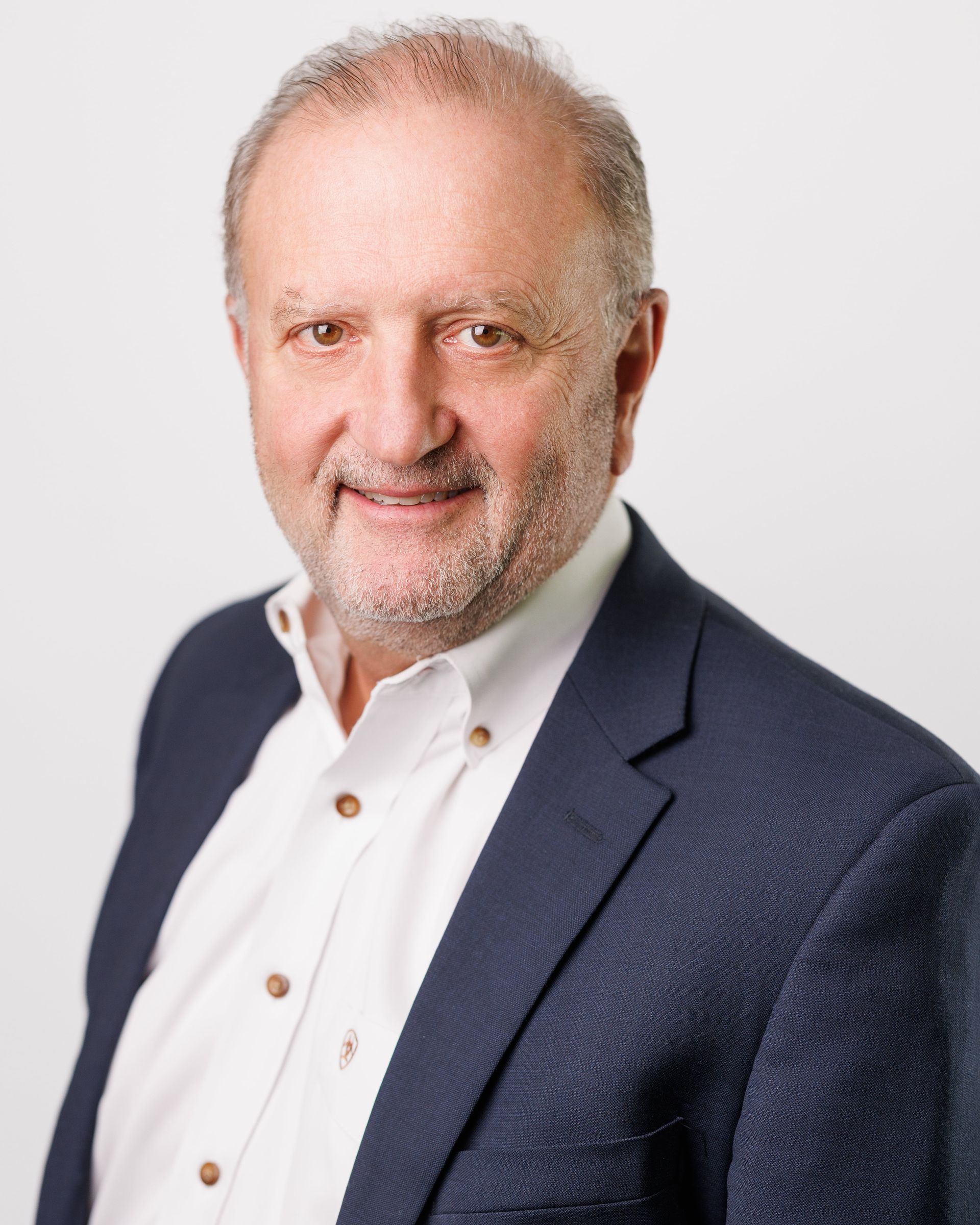 Man in navy blazer and white shirt, smiling at the camera.