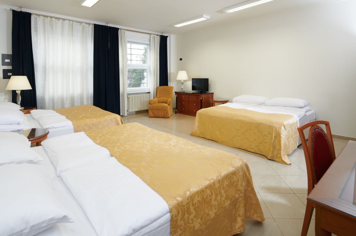 Una camera d'albergo con quattro letti, una piccola TV e una poltrona. Biancheria da letto gialla e bianca.