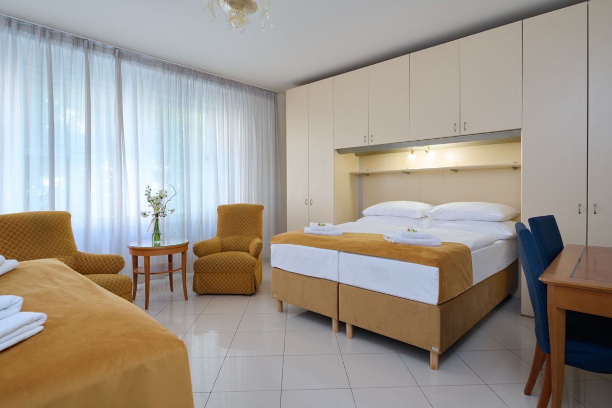 Camera da letto con due letti, due poltrone, tavolo e ampio armadio. Luce naturale, arredamento semplice.