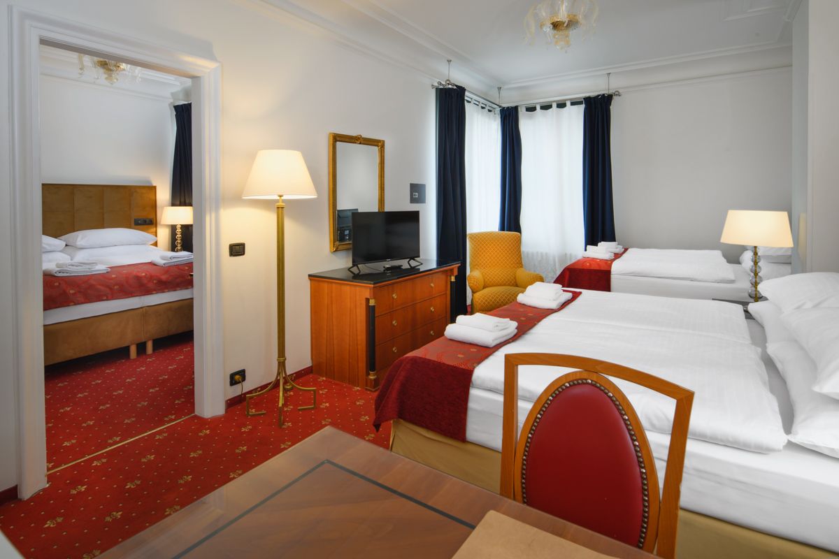Camera d'albergo con due letti, tappeto rosso e vista su una seconda camera da letto.