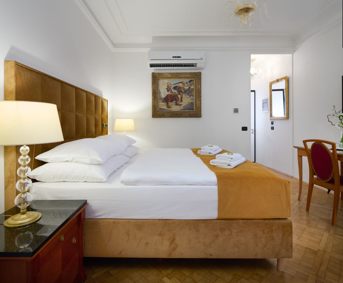 Camera d'albergo con letto, comodino, opere d'arte e uno sguardo su un'altra stanza.