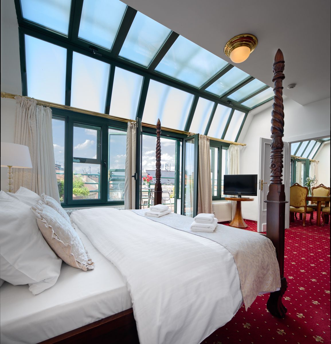 Camera da letto con letto a baldacchino, tappeto rosso e soffitto in vetro con vista sul cielo.