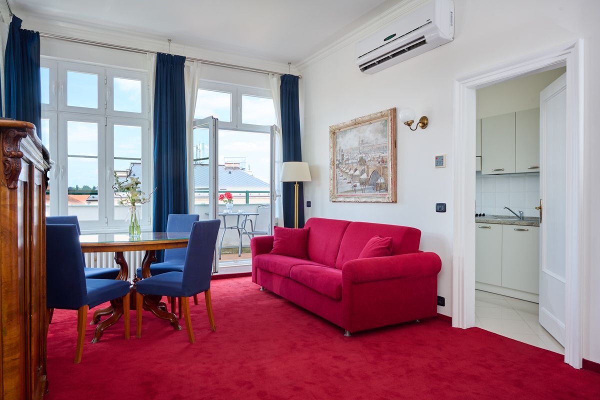 Soggiorno con tappeto rosso, divano, tavolo, sedie e accesso al balcone.