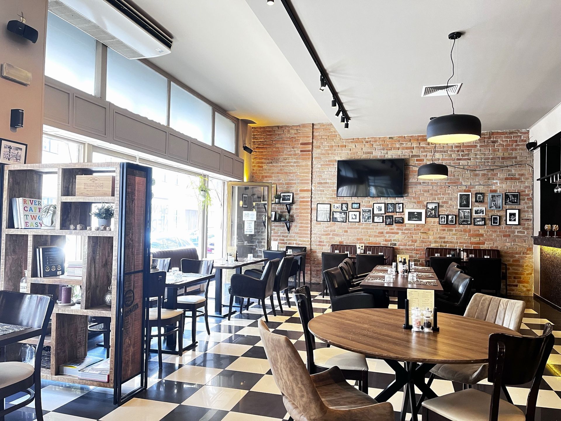 Interno di un ristorante con pareti in mattoni, pavimento a scacchi, tavoli e sedie.