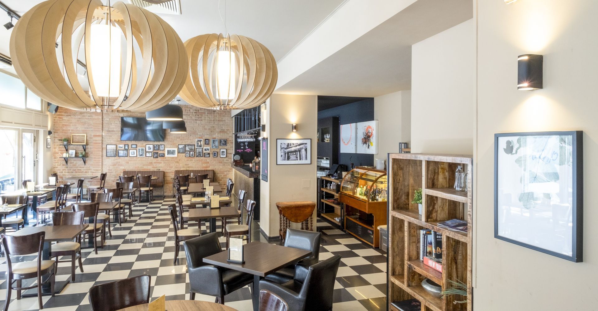 Interno del bar con pavimento a scacchi, tavoli, sedie e lampade a forma di globo.