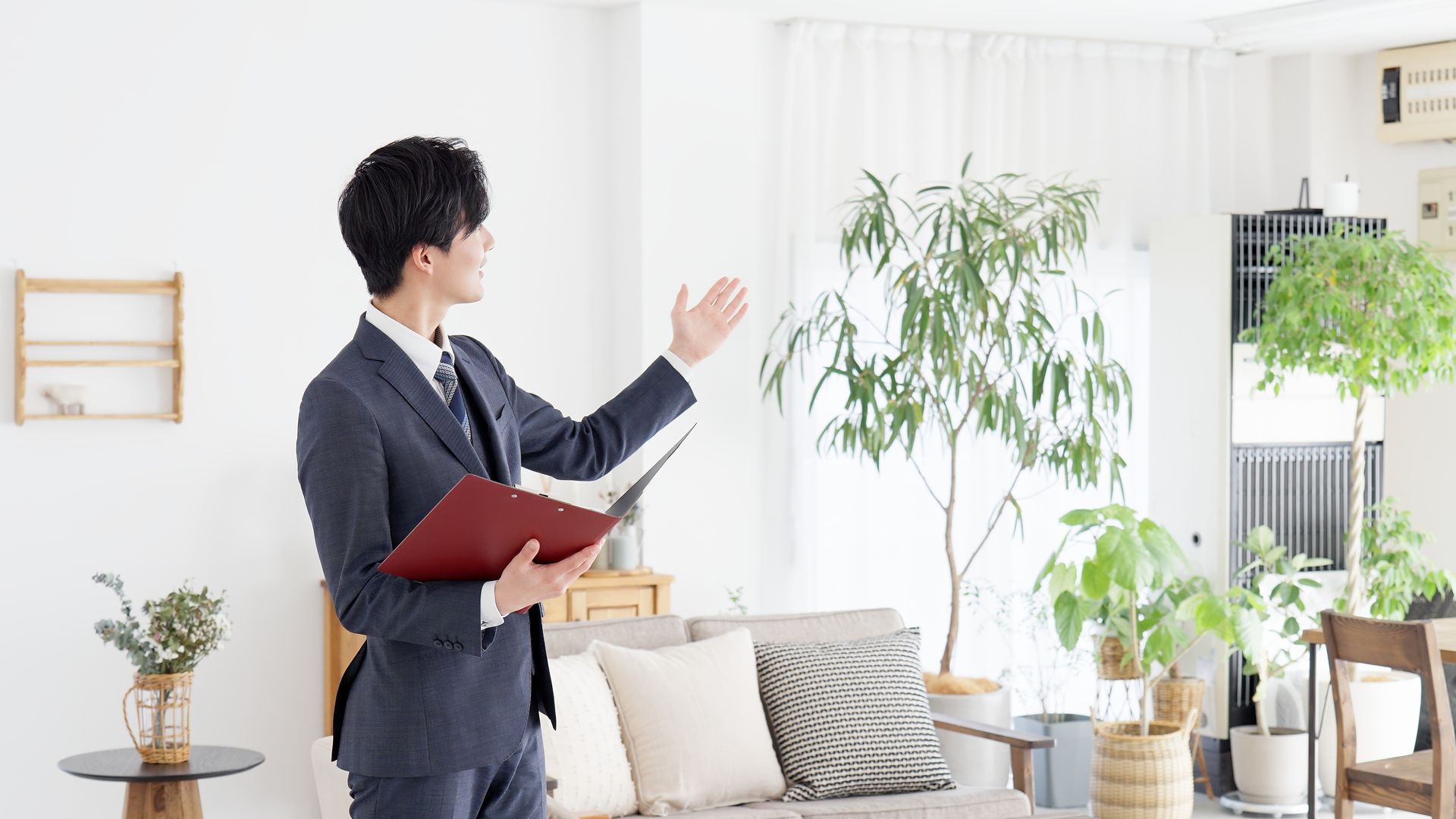 A man in a suit is standing in a living room holding a folder.