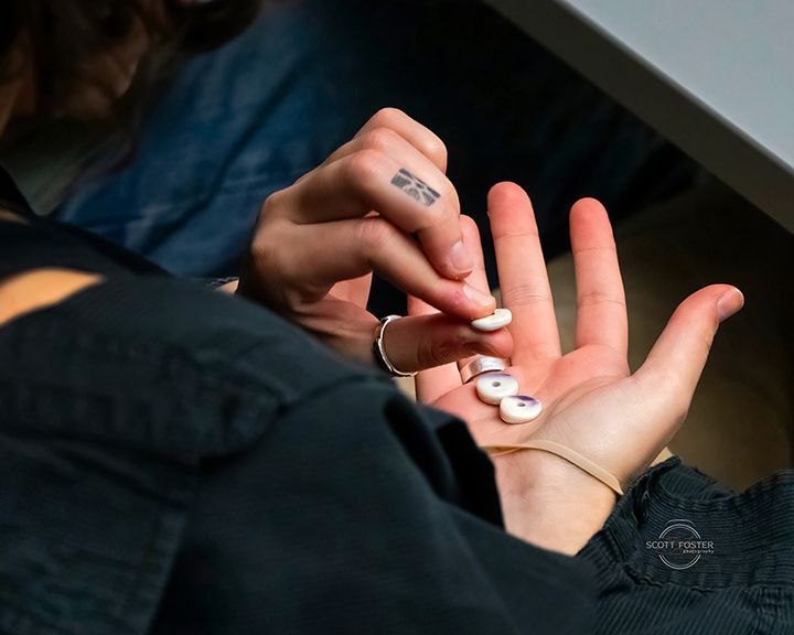Person holding white pills with a tattooed hand, possibly indoors.