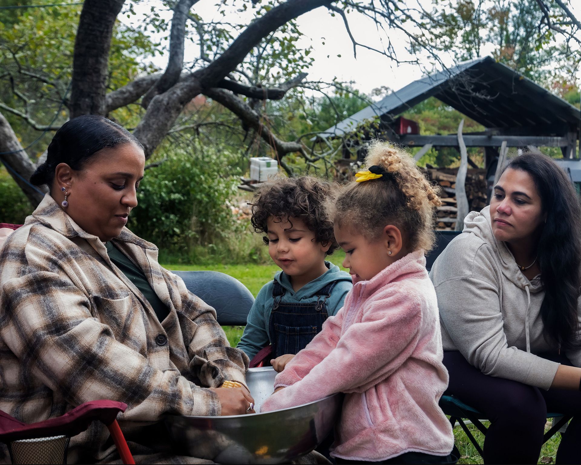 Family gathers outdoors; two children assist with mixing in a metal bowl.