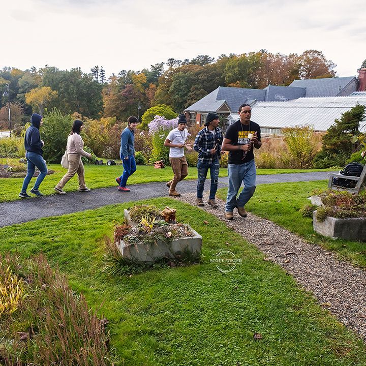 People walking on a garden path. Autumn trees and a building are in the background.