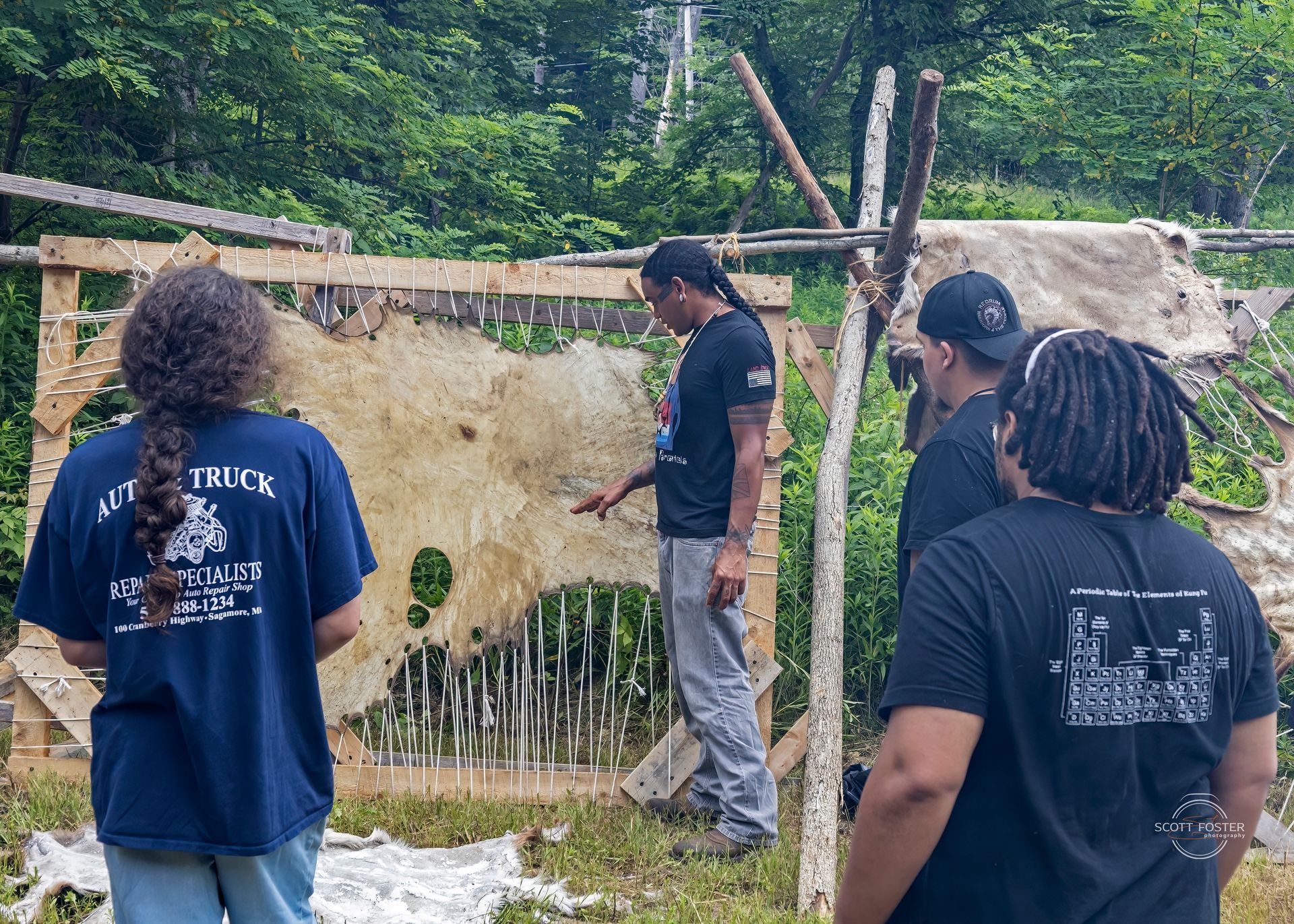 Group of people observing a stretched hide; outside, near trees. One points at the hide.