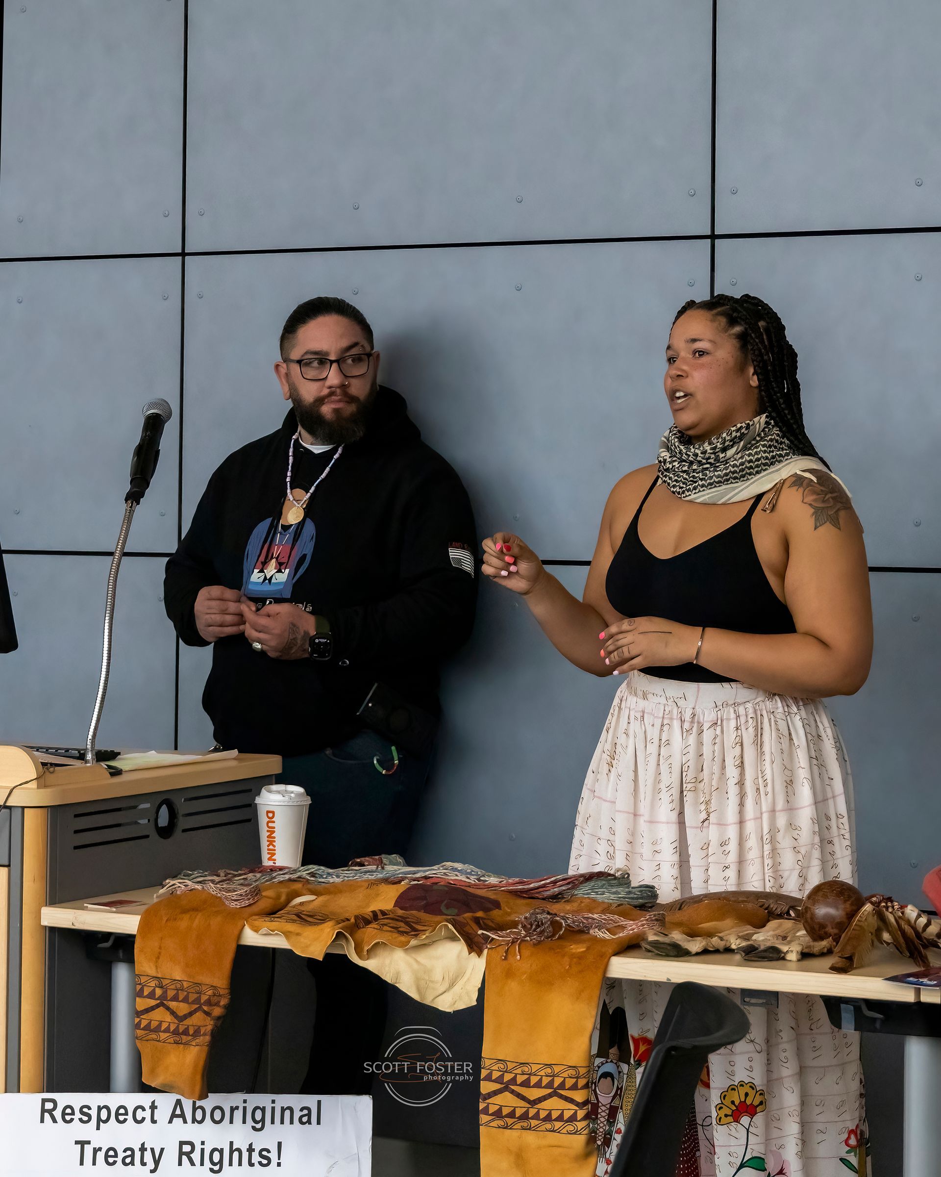 Two people speaking at a table with Indigenous artifacts. 
