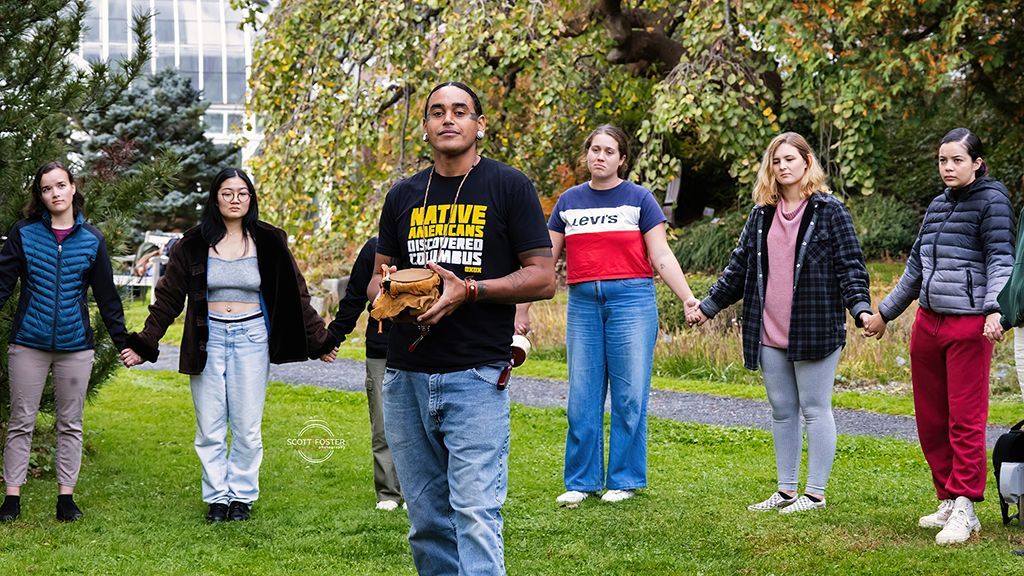 Group of people holding hands in a circle outdoors, one holding a wooden box.