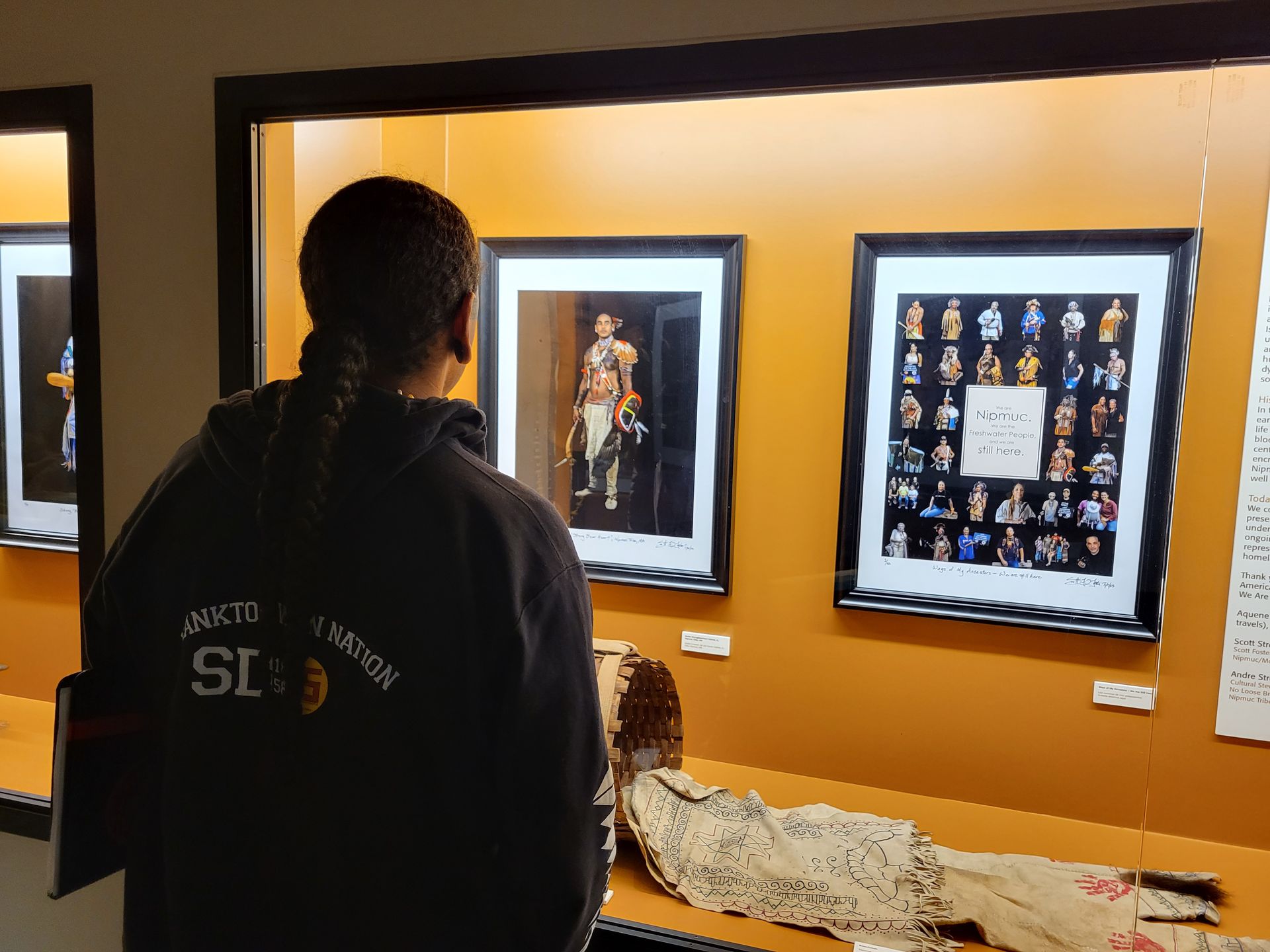Person looking at framed artwork in a museum display case with an orange background and a textile below.