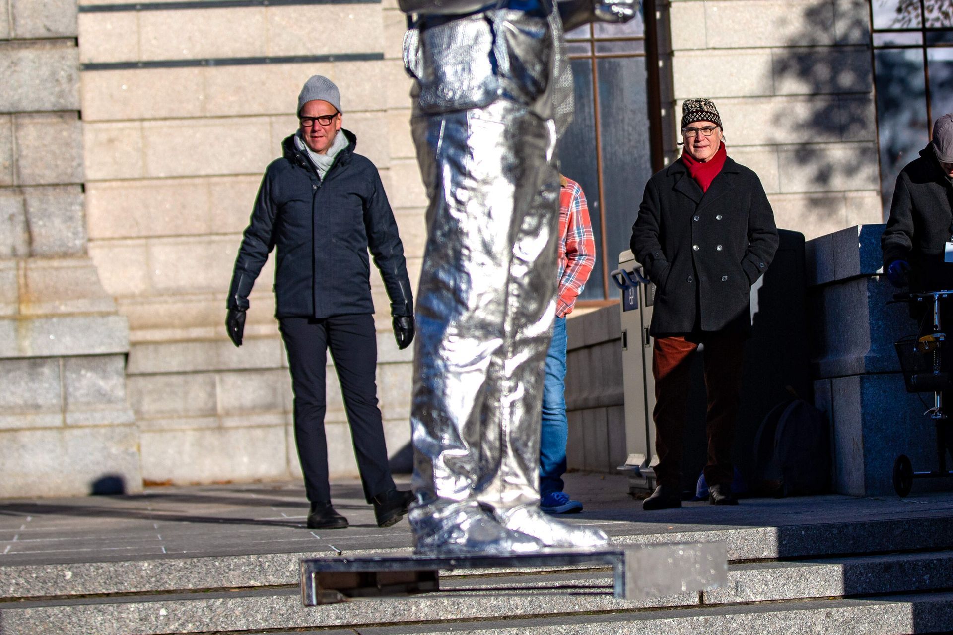 People standing near a street performer covered in silver foil; outside, sunny day.