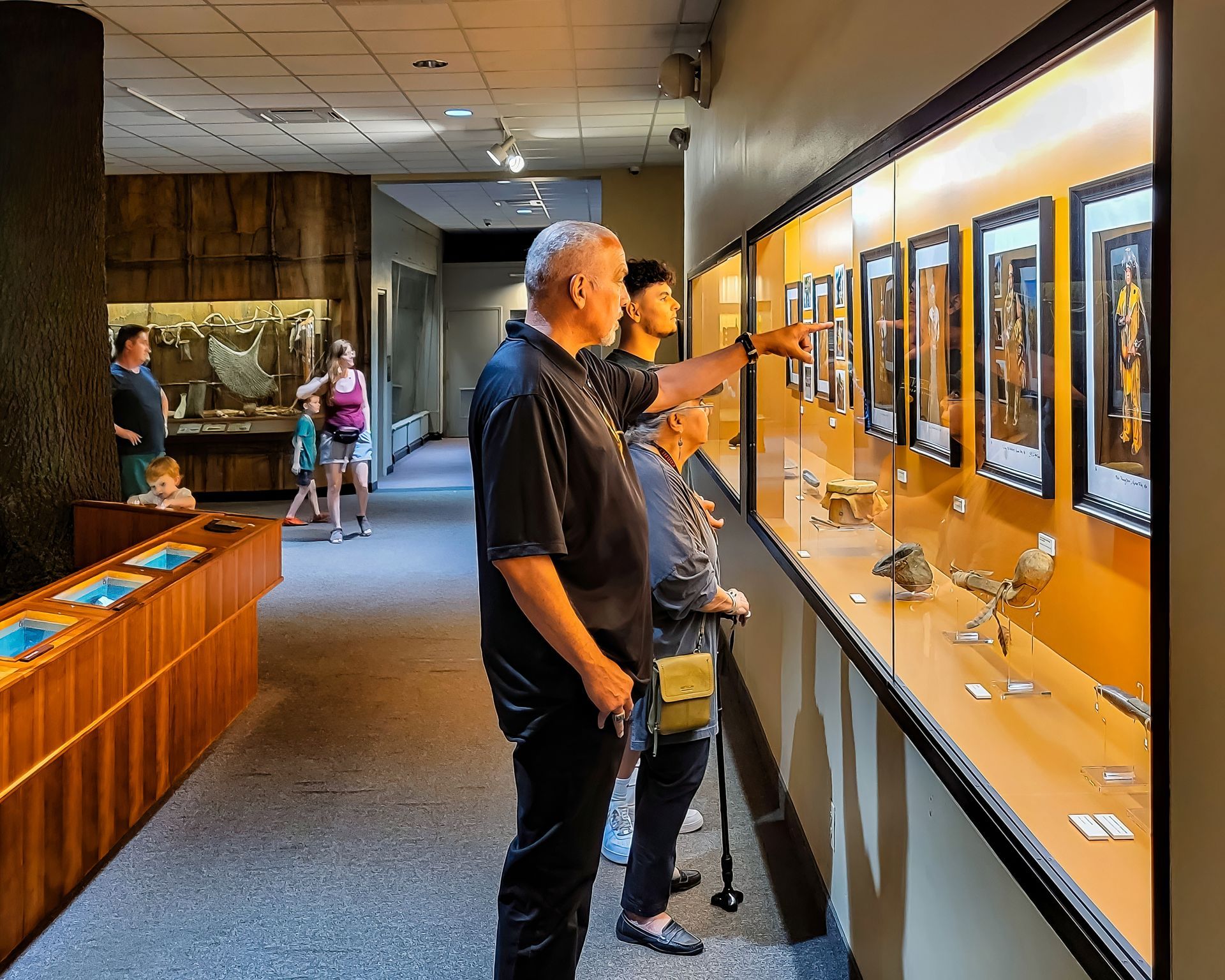 People in a museum looking at exhibits in display cases. Some are pointing and looking.