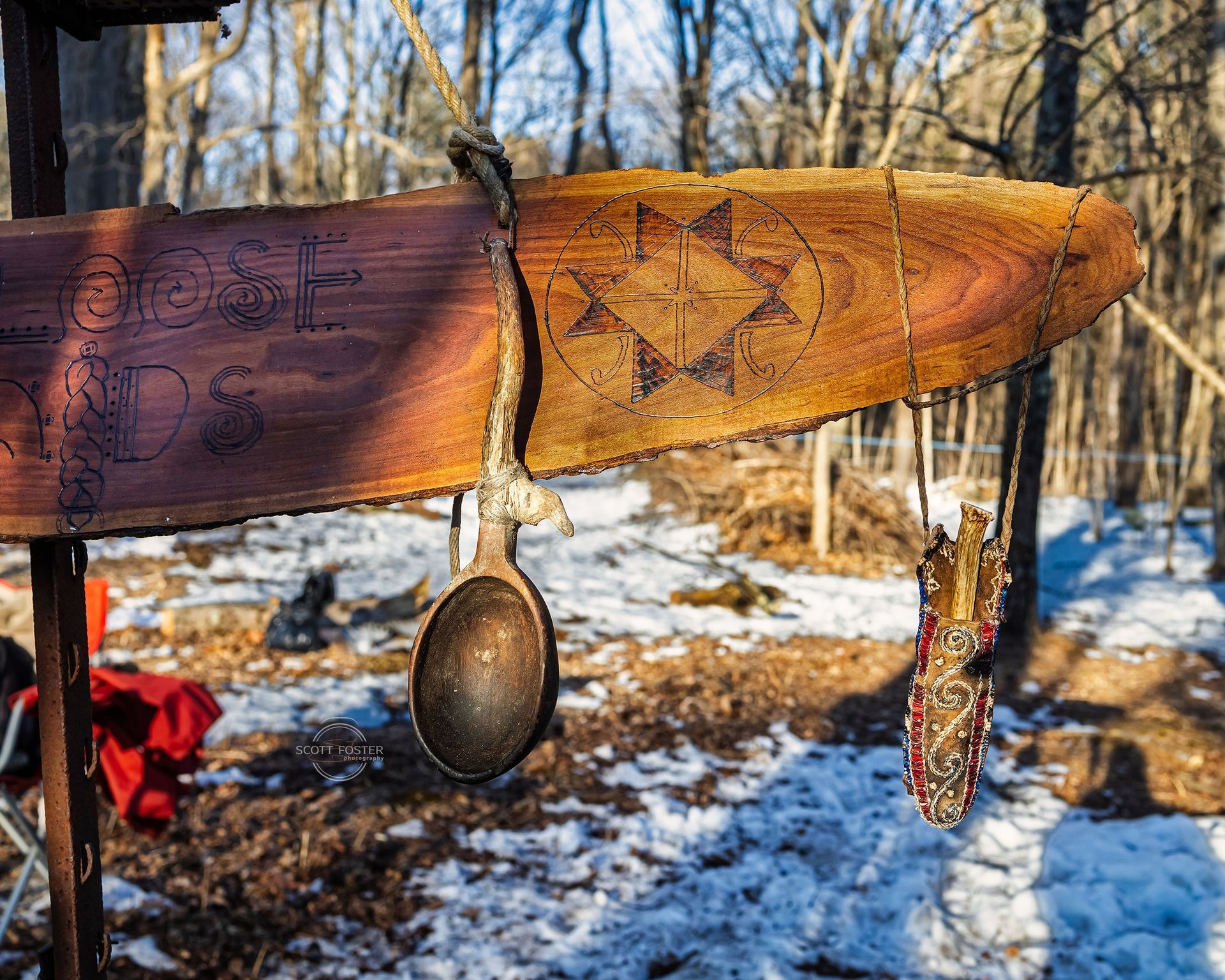 Wooden sign with burned design and spoon hanging. Snowy forest background.