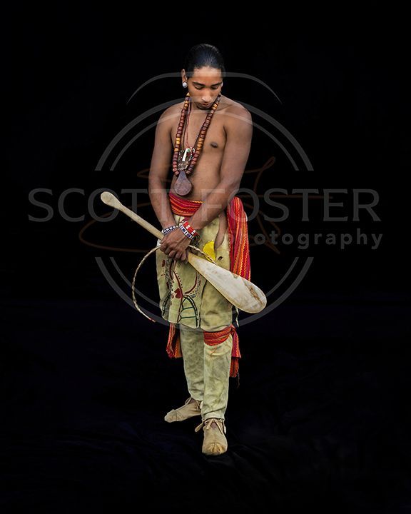 Man holding a club, wearing traditional clothing. Black background.