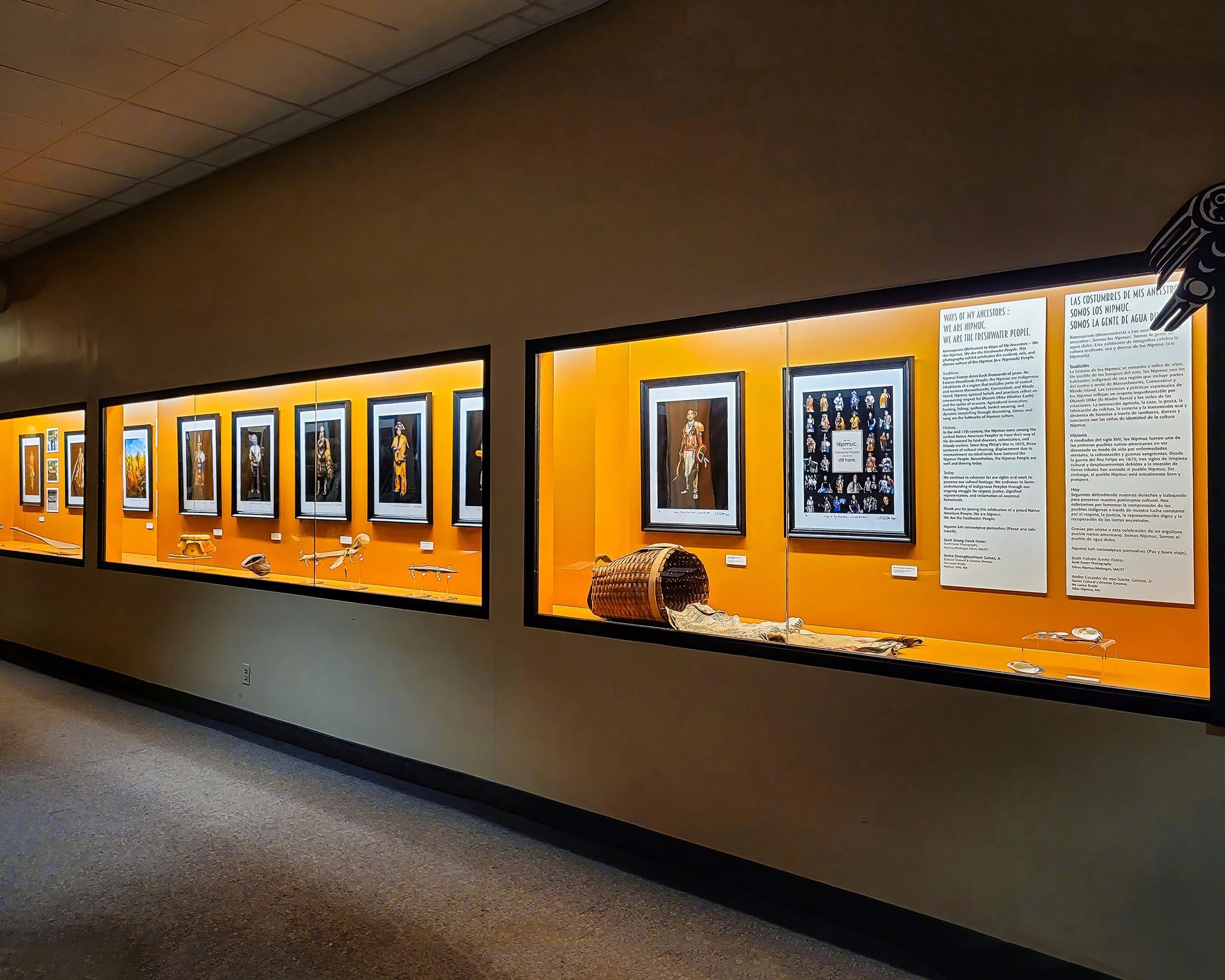 Museum display cases line a hallway. Photographs and artifacts are lit against an orange backdrop.