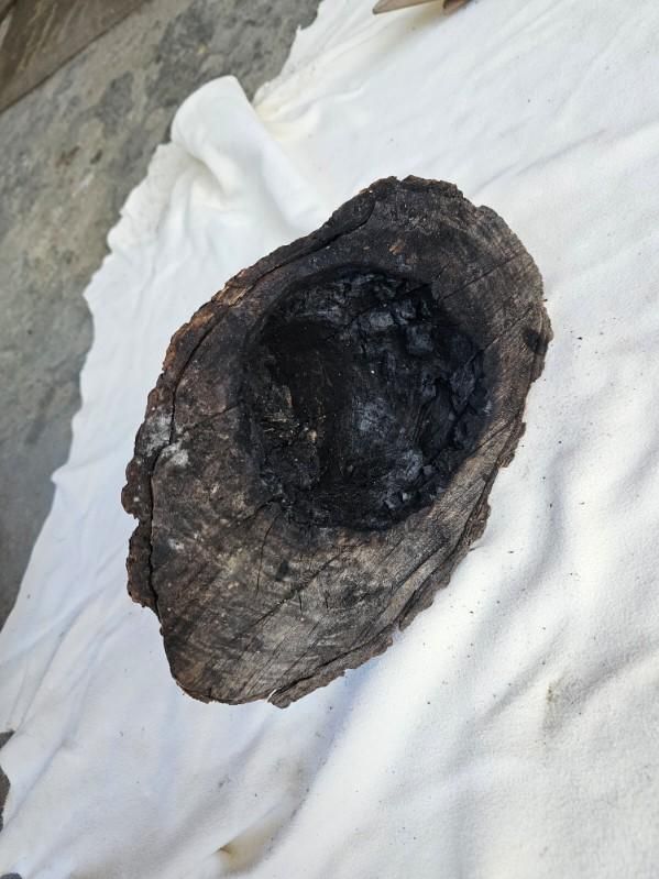 Charred wooden bowl, dark interior, resting on a white cloth.