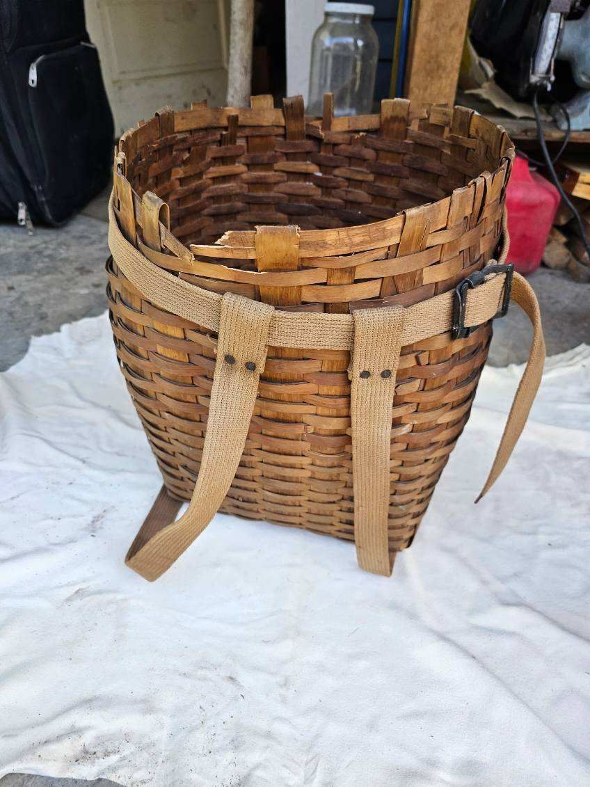 Woven brown backpack basket with tan straps and a black buckle, sitting on a white cloth.