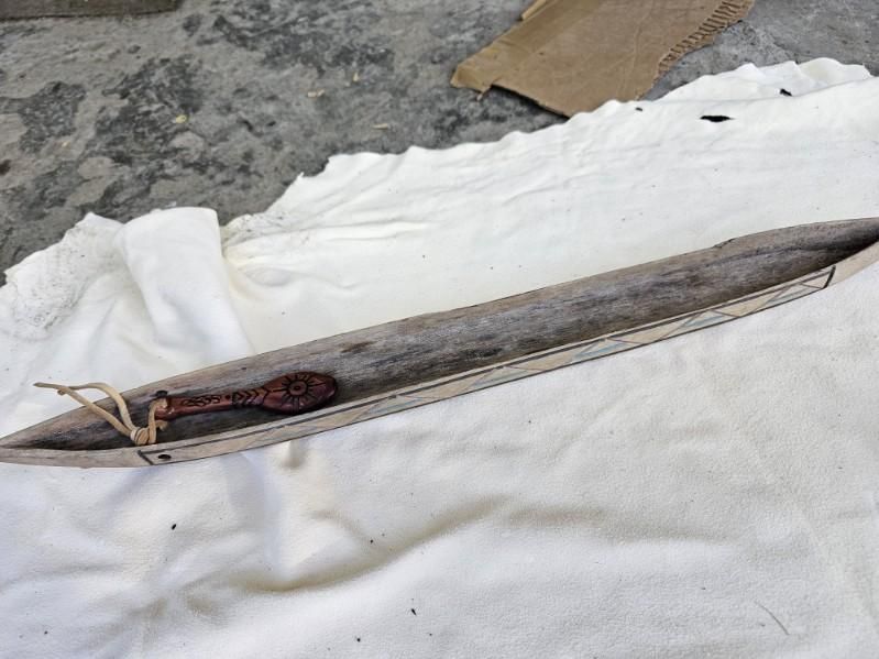 Long wooden trough with carved spoon inside, set on white fabric.