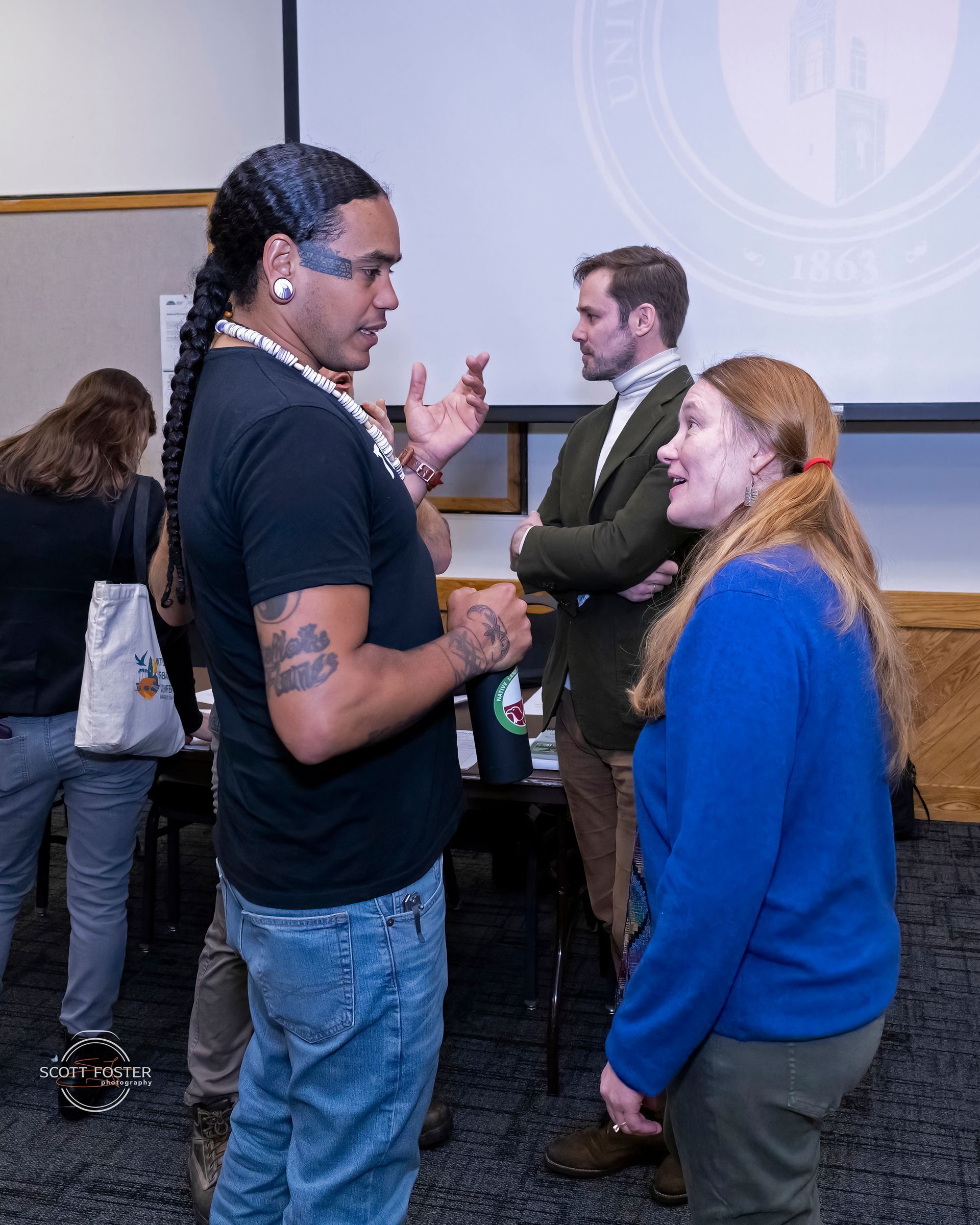 Man with face paint and woman in conversation; man in background.