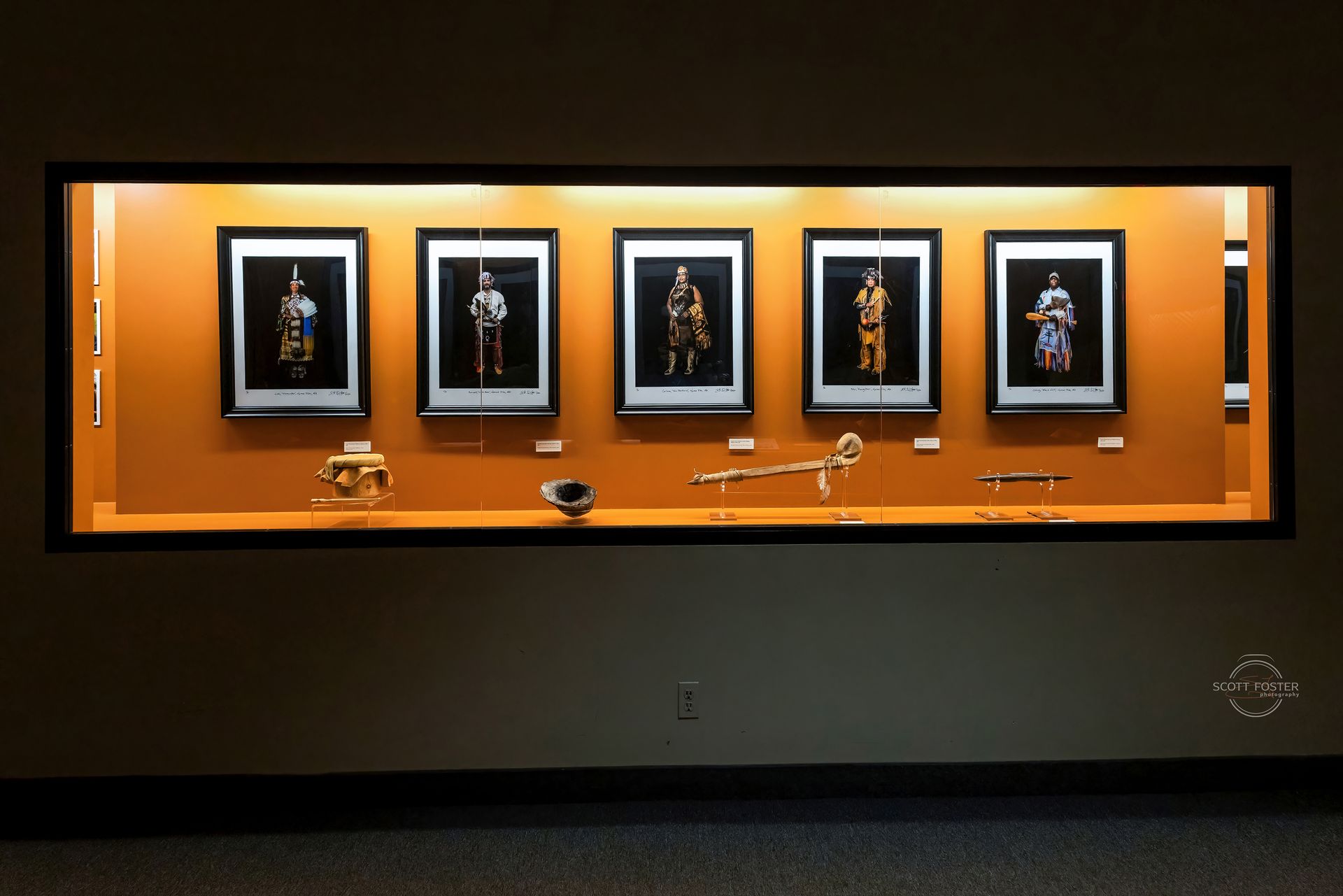 Display case with framed figures and artifacts, lit from above, against an orange background.