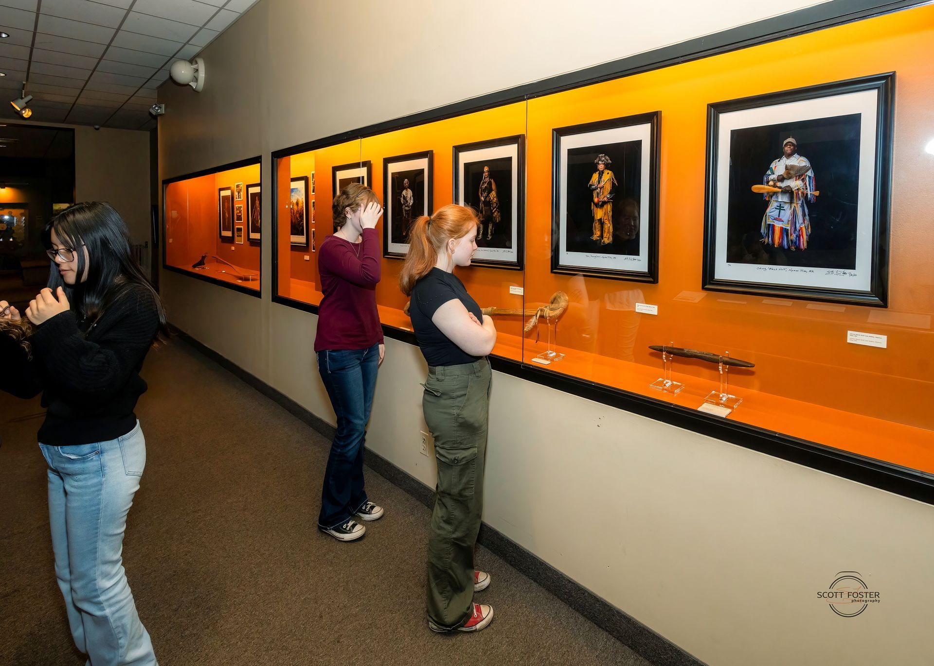 People viewing framed artwork and artifacts in a museum display.