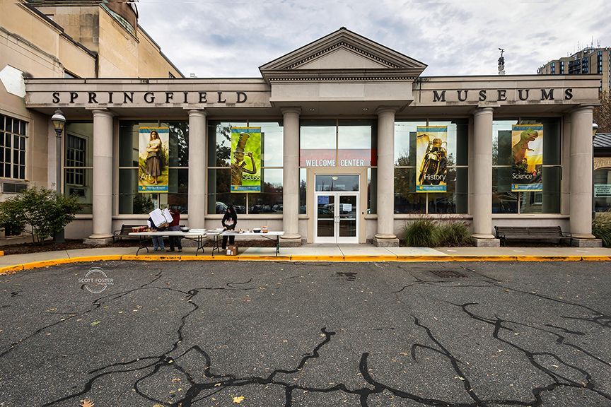 Springfield Museums entrance with pillars and posters. Two people at a table in front. Cloudy day.