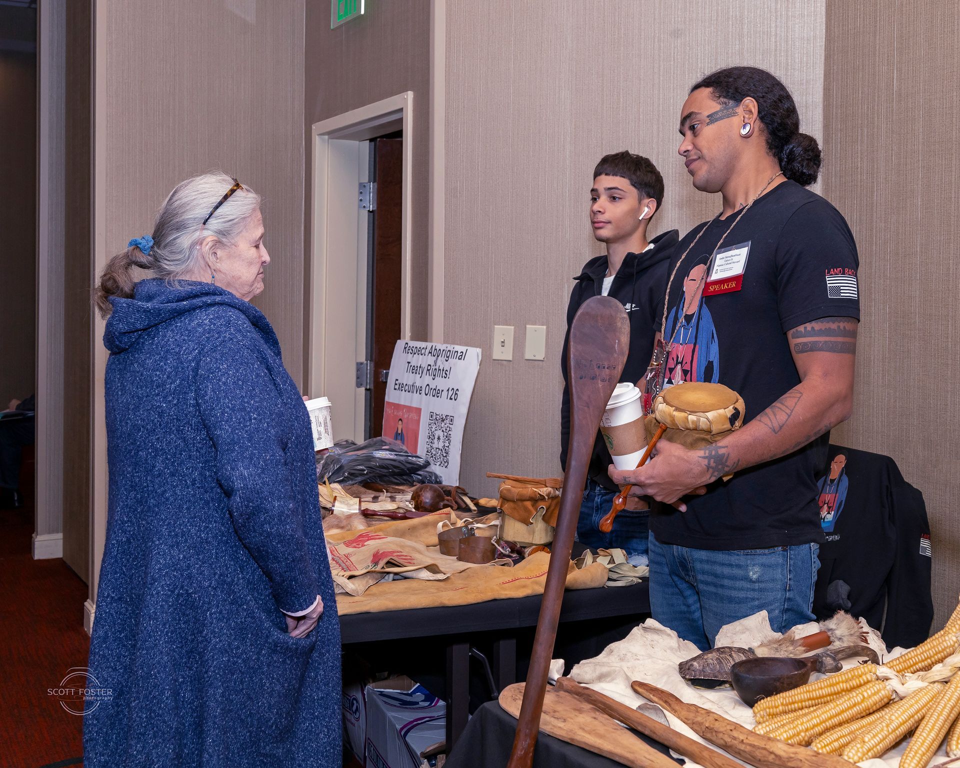 Woman speaking to two people at a table of handcrafted items in a conference room.