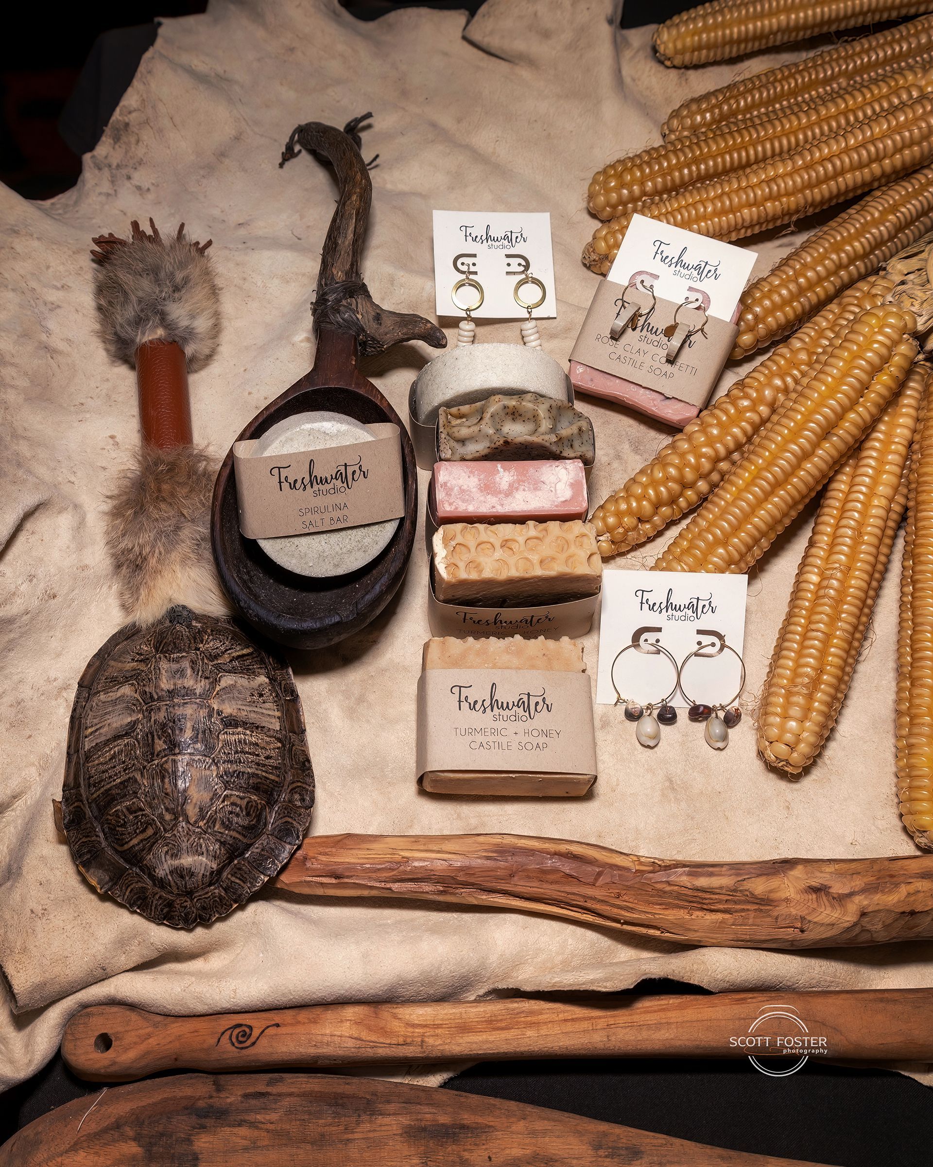 Collection of rustic items: soaps, corn, dried wood, turtle shell, and a feathered tool, likely for a market display.