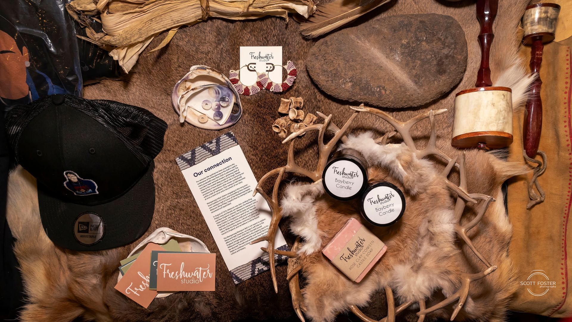 Display of handcrafted items: hats, earrings, soap, stones, deer antlers on a rustic fur surface.